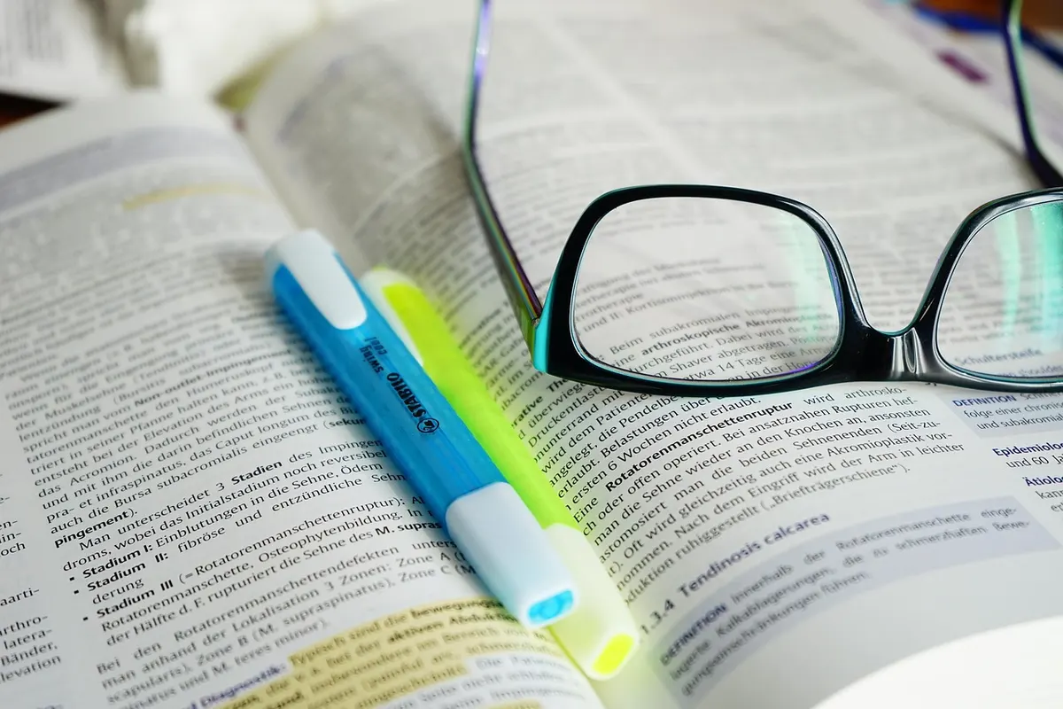 Highlighter pens and reading glasses resting on an open reference book, like an AI picking out the key lines from its sources.