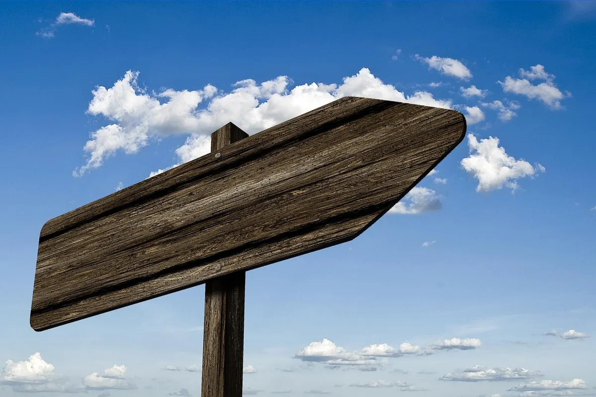 Wooden arrow-shaped signpost against a blue sky, pointing the way