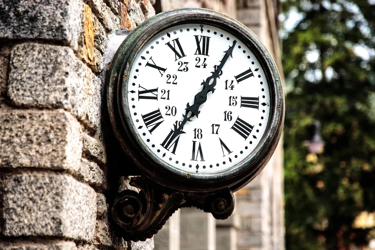 An old station clock with a 24-hour dial mounted on a stone wall, counting the hours a domain transfer can sit pending.