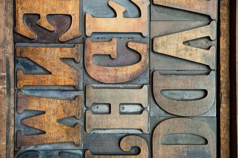Rows of old wooden letterpress letters in a printer's tray, the raw material for composing a business name.