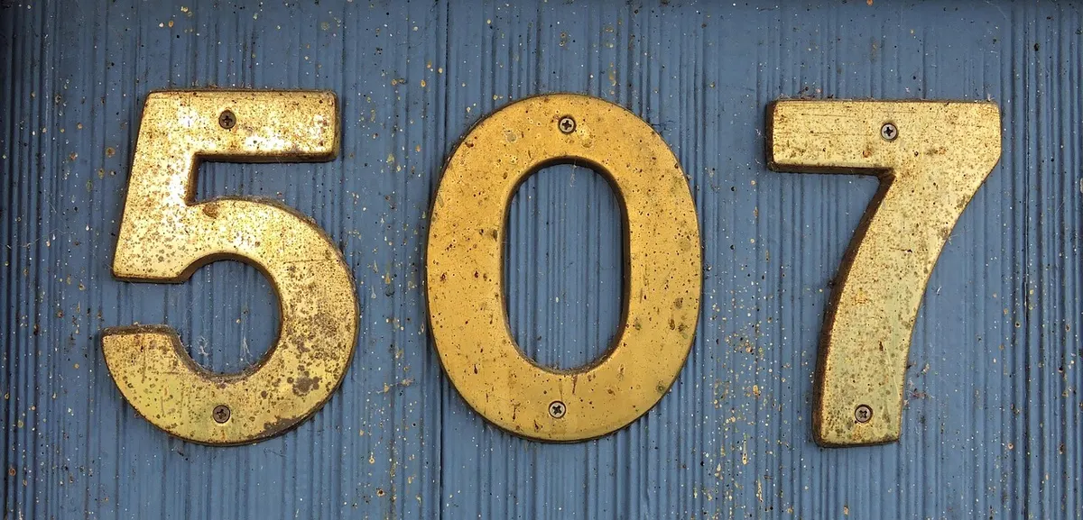 Brass house numbers reading 507 screwed to a blue wooden wall, a reminder that an address only works if it's exactly right.