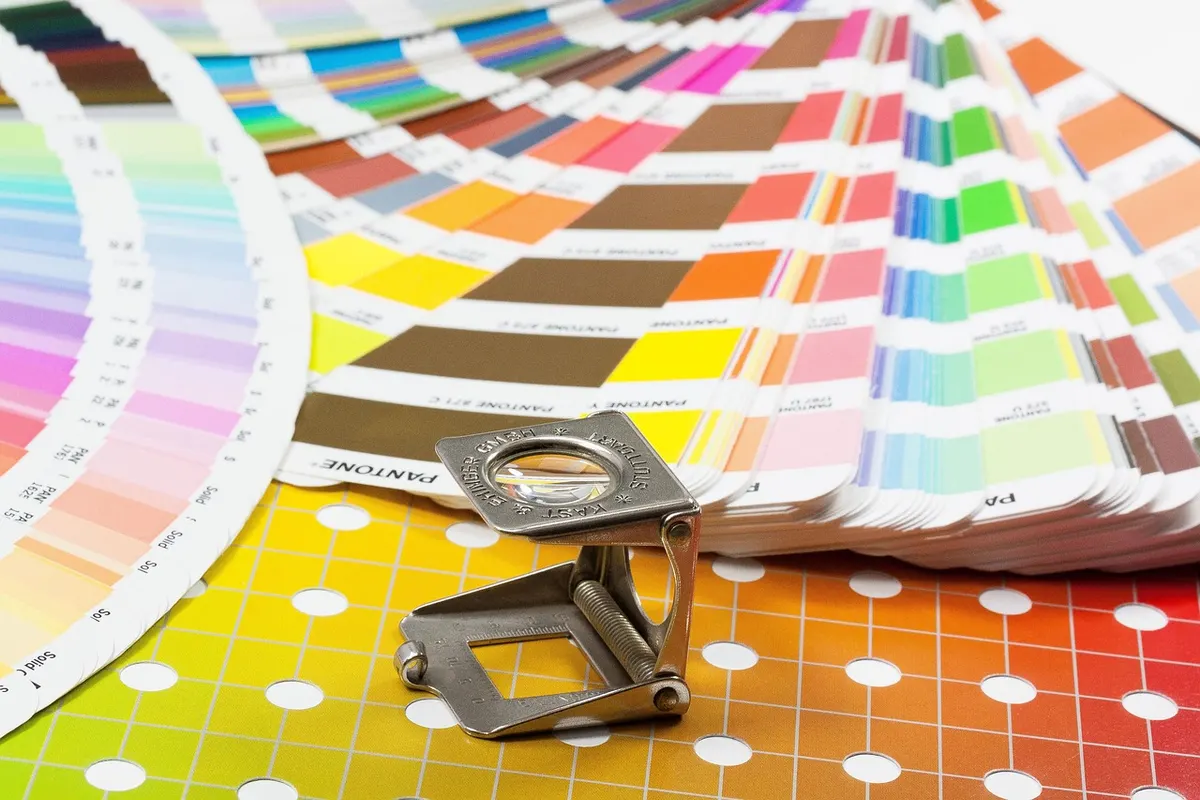 A printer's colour swatch fan with a magnifying loupe resting on it, the kind of exact colour reference a brand style guide records.