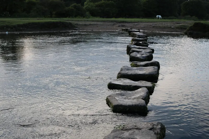 A line of stepping stones crossing a calm river at dusk, a picture of building links one at a time.