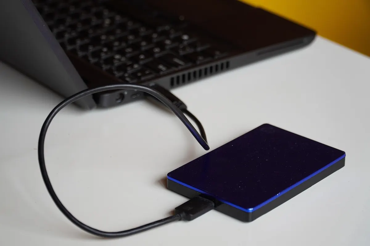 A slim external hard drive plugged into a laptop by its cable, the kind of separate copy every website backup needs.