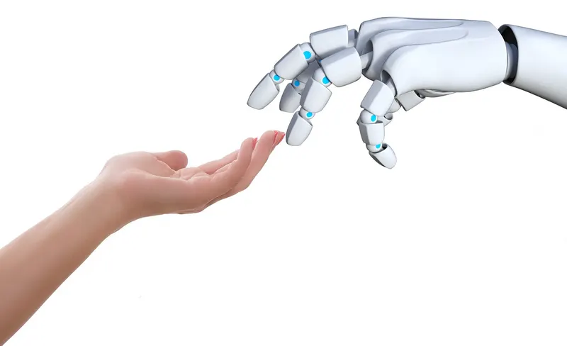 A human hand and a white robotic hand reaching towards each other against a plain background.