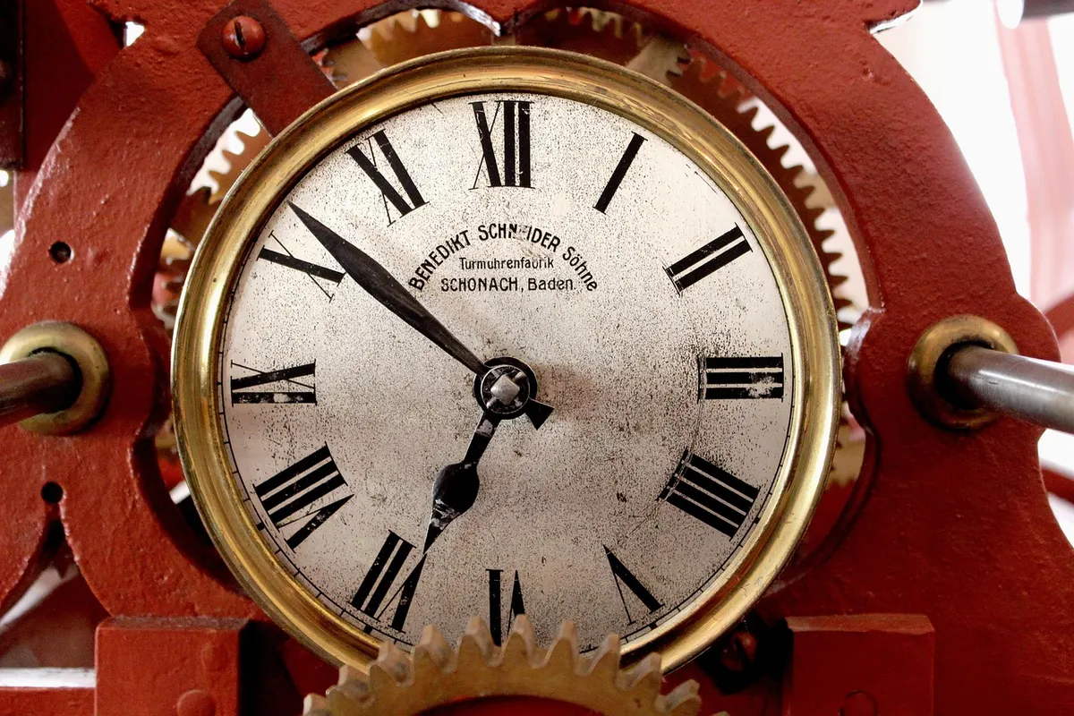 Close-up of an old tower clock face with its iron gears and frame visible, keeping time without a break.