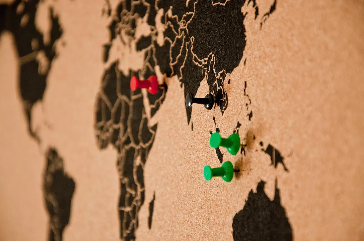 A cork world map with coloured push pins marking locations, like choosing where a website's server should sit.