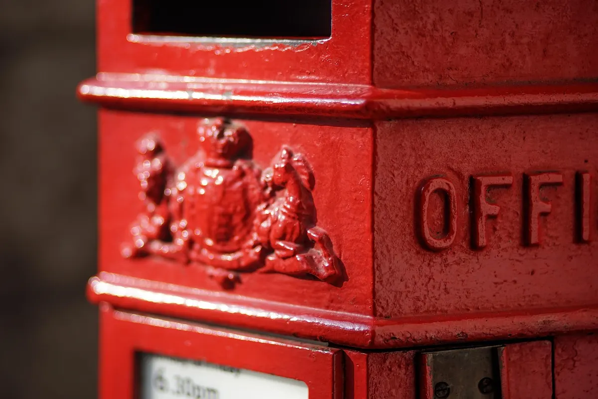 Close-up of a classic red British post box with a raised royal crest, as recognisably British as a .co.uk address.