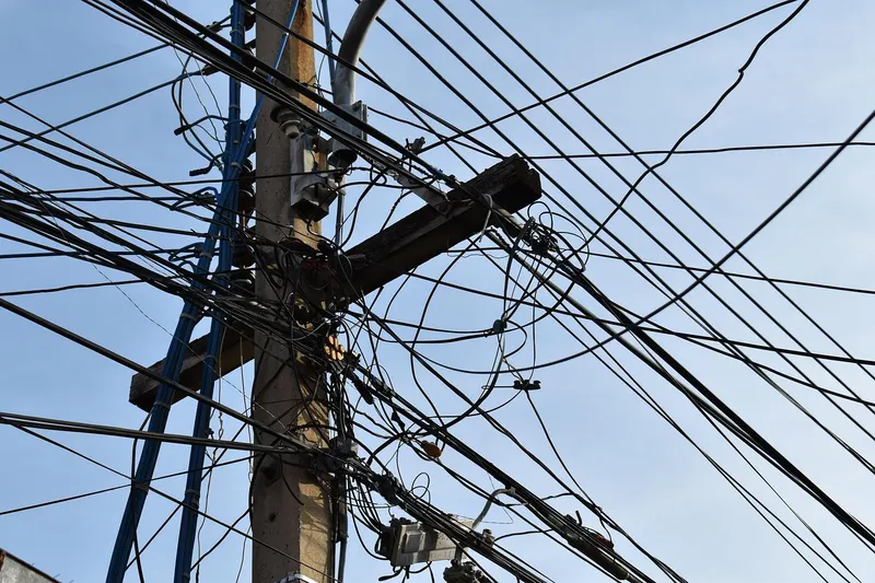 Tangled mess of electrical cables on a telegraph pole against a blue sky