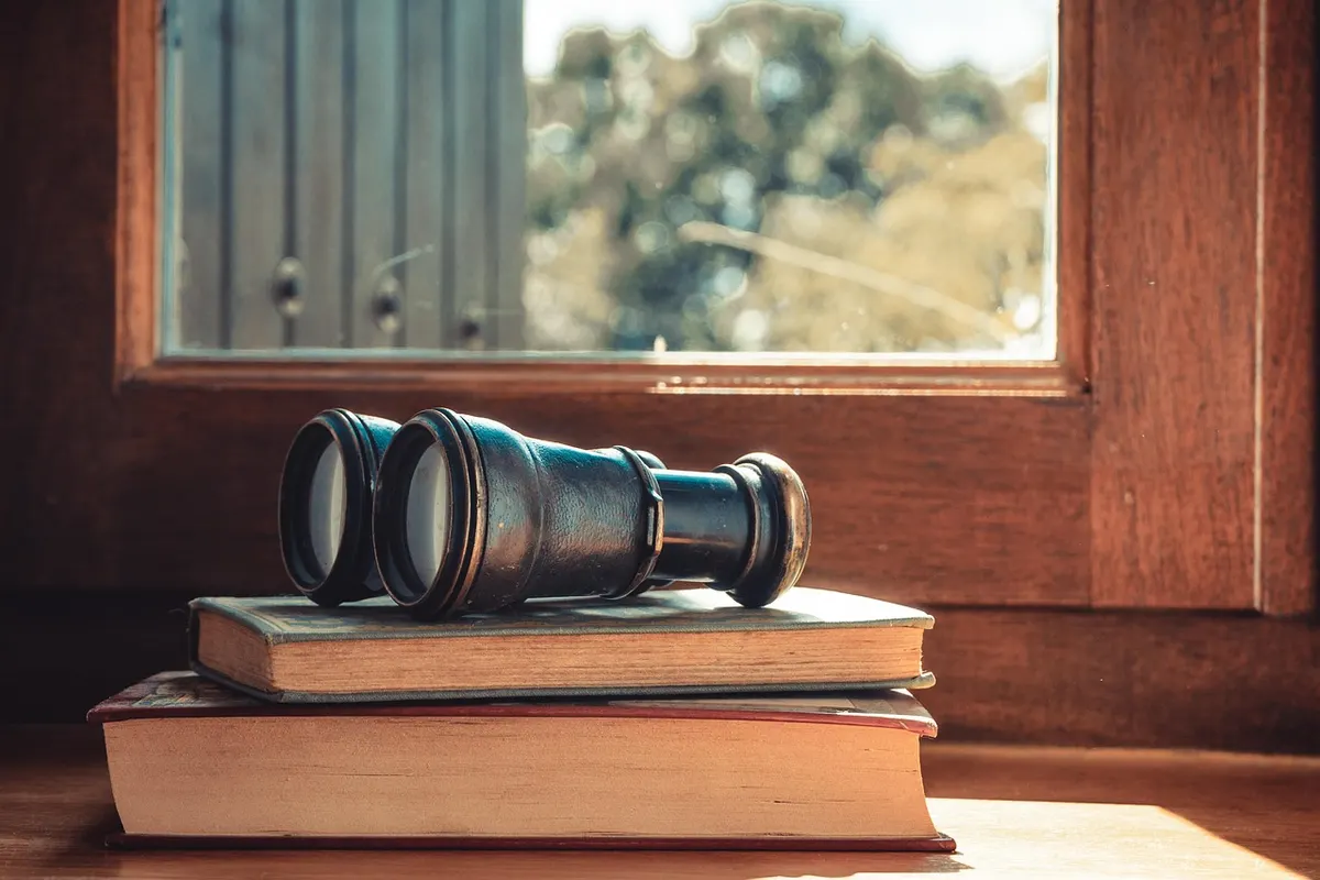 A pair of old binoculars resting on a stack of books by a sunny window, ready for a bit of detective work.