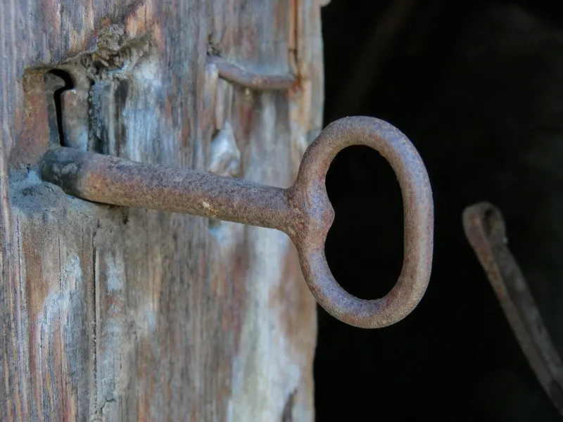 An old iron key in a rustic wooden door lock