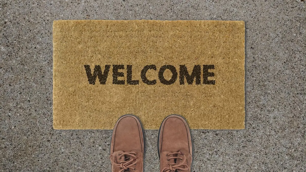 A pair of brown shoes standing on a doormat that says Welcome, the spot where a visitor first arrives.
