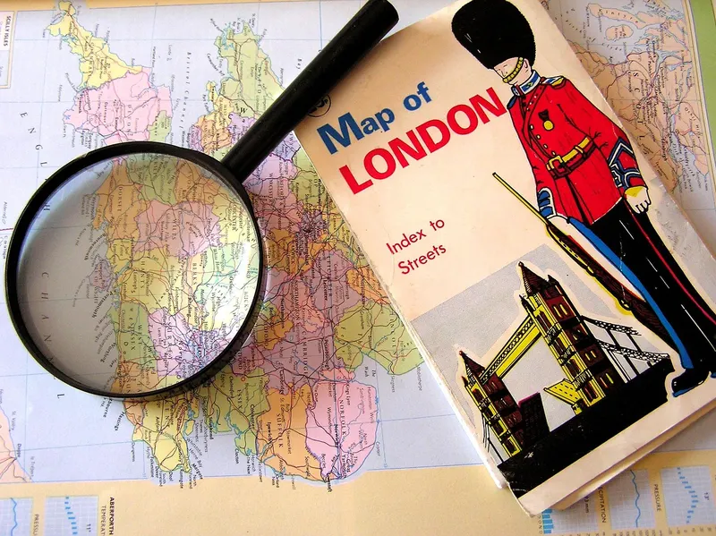 A magnifying glass resting on a map of England beside a folded Map of London, like searching for a business that should be there.