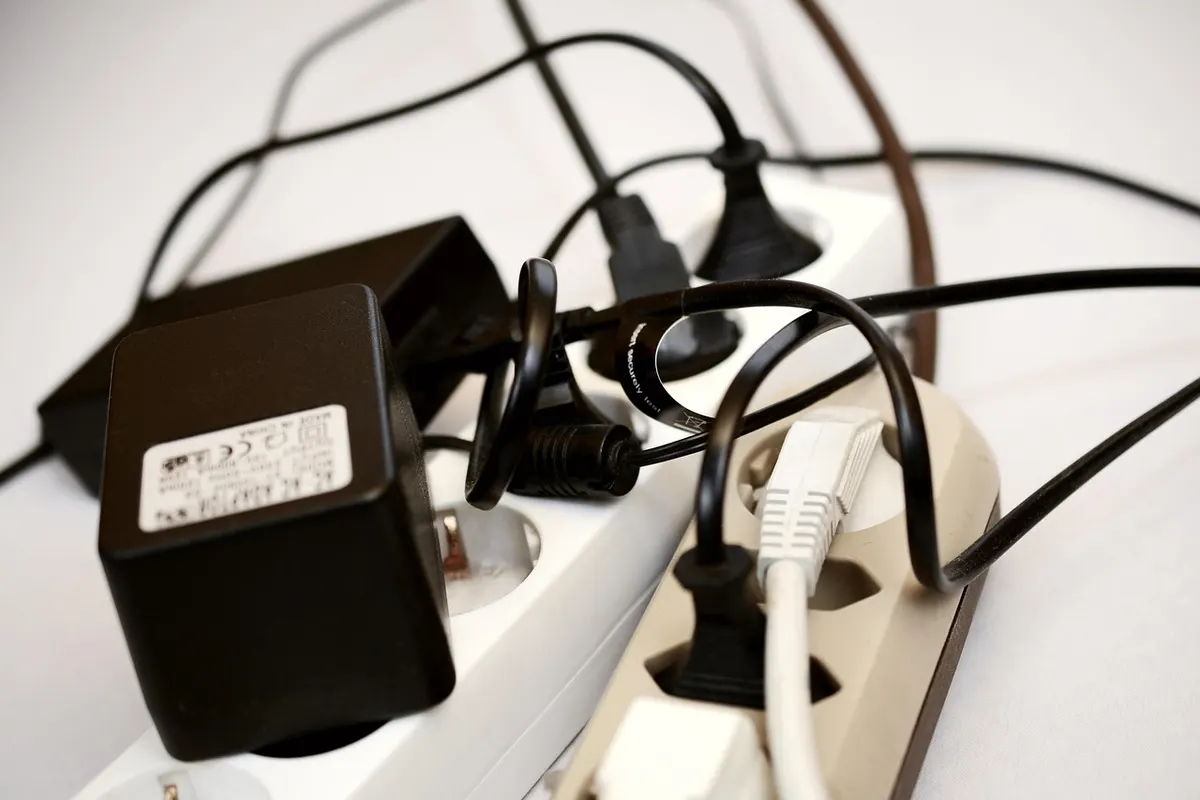 A white power strip crowded with plugs and a bulky adapter, cables tangled across it.
